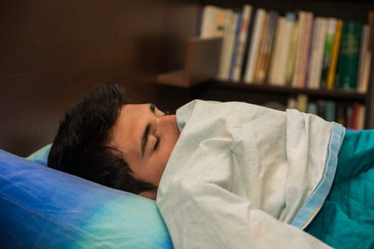 A man laying on a bed with a pillow. Photo of a handsome young man resting on a comfortable bed with a soft pillow. Only his eyes are visible.