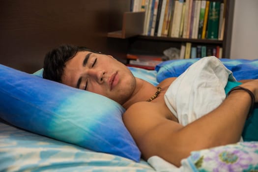 A man laying on a bed with a pillow. Photo of a handsome young man resting on a comfortable bed with a soft pillow