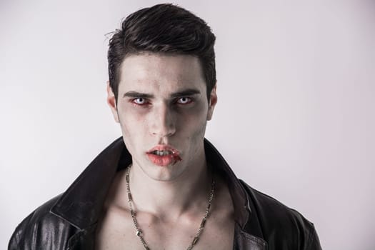 A man wearing a necklace with blood on his face. Photo of a handsome young man with blood on his face wearing a vampire necklace