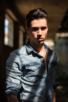 A man standing in an alley with his hands in his pockets in an abandoned building, looking at camera