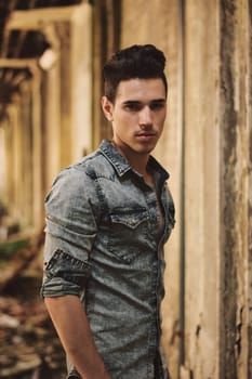 A man standing in an alley with his hands in his pockets. Photo of a man standing in an alley with his hands in his pockets in an abandoned building, looking at camera