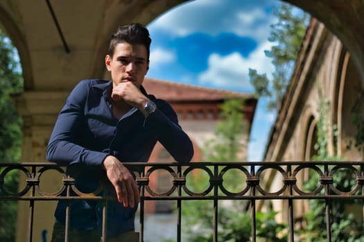 A man leaning on a fence with his hand on his chin. Photo of a pensive man leaning on a fence, deep in thought