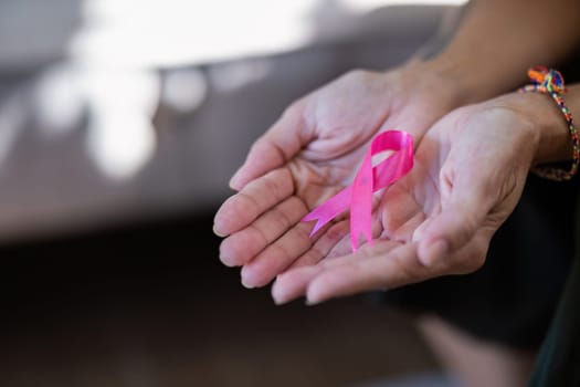 Elder woman hand holding pink ribbon symbol. Breast cancer awareness and october pink day, world cancer day, national cancer survivor day. healthcare concept.