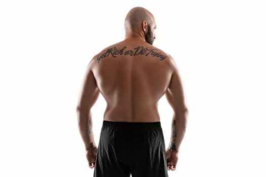 Good-looking bald, bearded, tattooed person in black shorts is posing standing back to the camera and showing his muscles, isolated on white background. Chic muscular body, fitness, gym, healthy lifestyle concept. Close-up portrait.