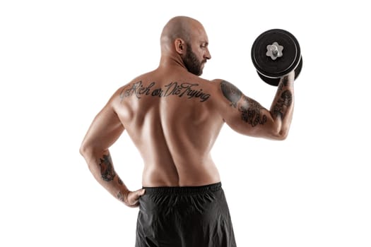 Strong bald, bearded, tattooed person in black shorts is posing with a dumbbell in his hand, standing back, isolated on white background. Chic muscular body, fitness, gym, healthy lifestyle concept. Close-up portrait.