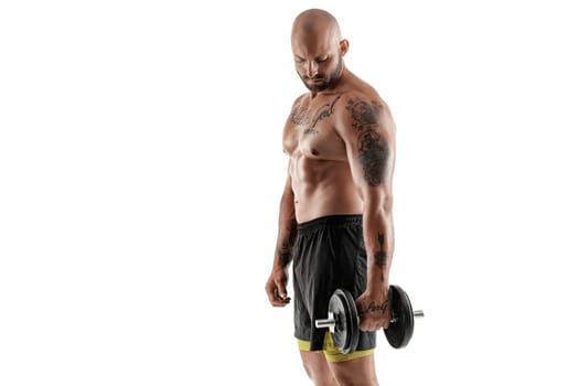 Masculine bald, bearded, tattooed fellow in black shorts is posing standing sideways, with a dumbbell in his hand, isolated on white background. Chic muscular body, fitness, gym, healthy lifestyle concept. Close-up portrait.
