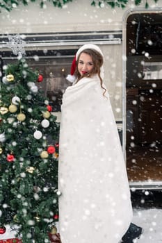 Young woman in santa costume decorates the Christmas tree at winter campsite getting ready for the new year. New year celebration concept