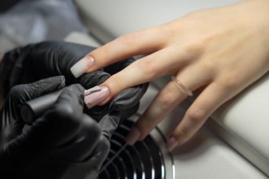 Female hands and tools for manicure, process of performing manicure in beauty salon. Nail care procedure in a beauty salon. Gloved hands of an experienced manicurist in gloves are varnished nails