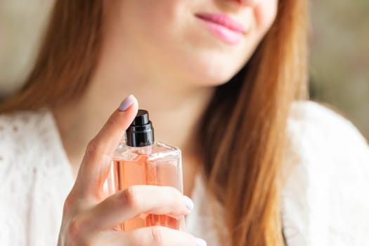 Beautiful young woman with bottle of perfume spraying it on her neck at home.