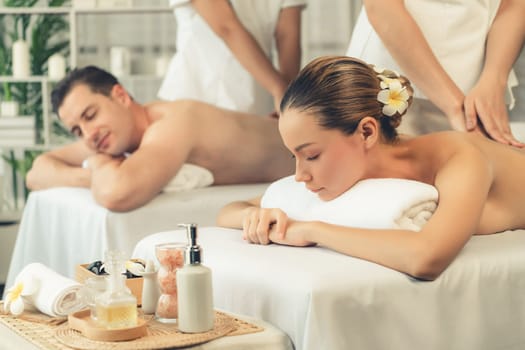 Caucasian couple customer enjoying relaxing anti-stress spa massage and pampering with beauty skin recreation leisure in day light ambient salon spa at luxury resort or hotel. Quiescent