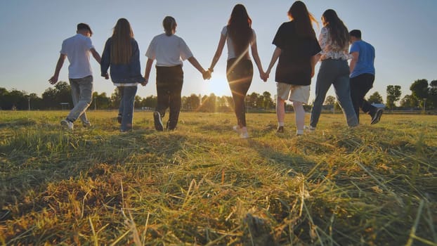 Friends at sunset holding hands walking towards the sun