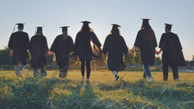 College graduates hold hands at sunset to meet the future and the sun