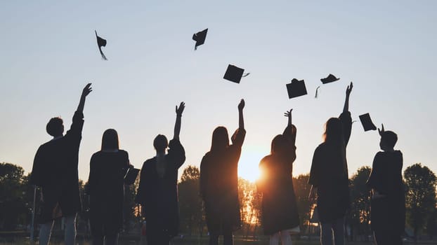 Silhouettes of Happy college graduates tossing their caps up at sunset