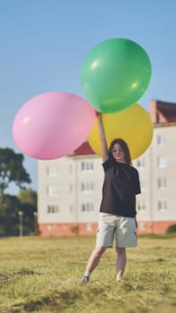 A girl happily poses with large with colorful balloons in the city. Vertical video for smartphone