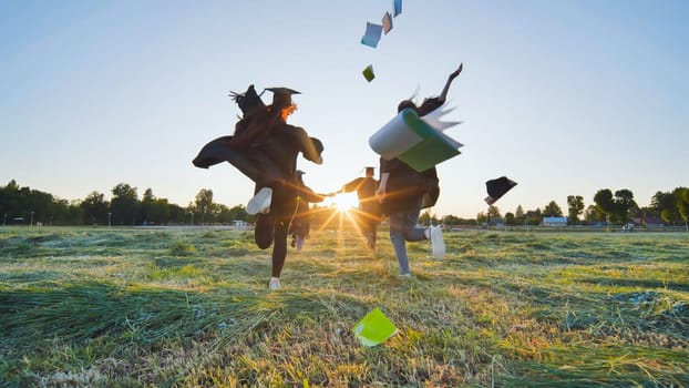 Cheerful graduates students run throwing notebooks after school at sunset