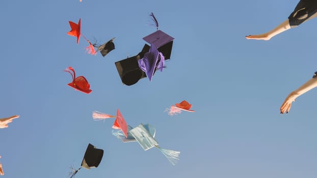 Happy college graduates standing in a circle tossing colorful hats up