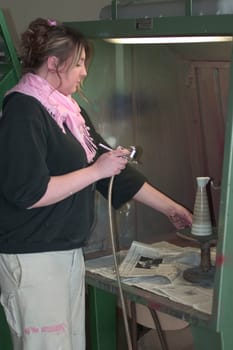 Vocational school student painting a porcelain container with spraying technique