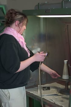 Vocational school student painting a porcelain container with spraying technique