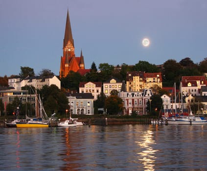 Jürgensby (district of Flensburg) is illuminated by the evening sun and at the same time the moon is reflected in the water.