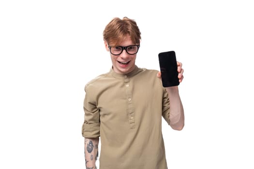 young cheerful optimist handsome man with copper hair with a tattoo on his arm shows the smartphone screen.