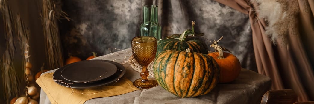 Autumn interior: a table covered with dishes, pumpkins, a relaxed composition of Japanese pampas grass. Interior in the photo Studio. Close - up of a decorated autumn table.