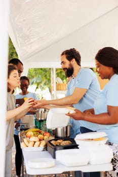 Group of volunteers smiles while providing humanitarian aid to needy at non-profit food drive event. Charitable individuals supporting and sharing nourishments to homeless and less fortunate people.