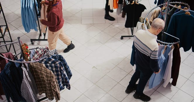 Top down view of clients walking around bustling shopping mall fashion shop aisles, looking to purchase clothes as presents for family and friends during Christmas promotional sales event