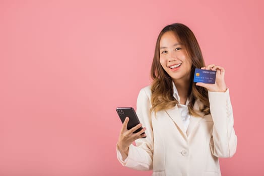 Happy Asian portrait beautiful cute young woman excited smiling hold mobile phone and plastic debit credit bank card, studio shot isolated on pink background, female using smartphone online shopping