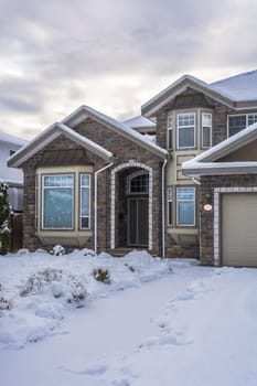 Entrance of big luxury house with front yard in snow. Residential house on winter cloudy day