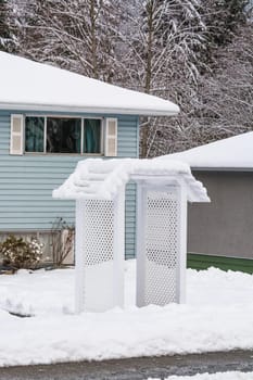 Residential house front yard in snow with entrance arch over pathway. Average North American house on winter cloudy day