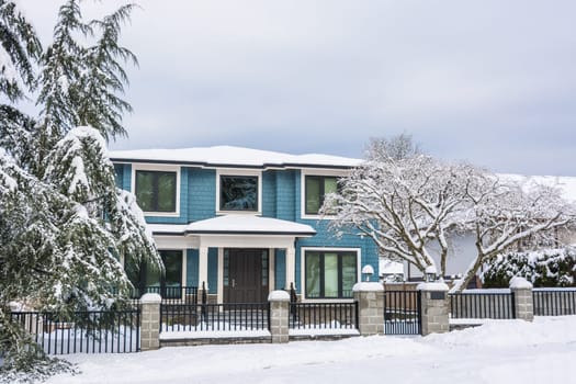 Entrance of family house with metal fence and front yard in snow. Residential house on winter cloudy day