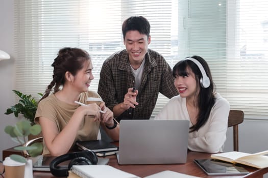 A cheerful and intelligent young Asian man is standing and sharing his thoughts in a meeting with his team. University students, friendship, startups, teamwork.