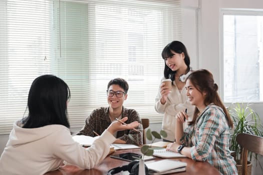 A cheerful and smart young Asian female is standing and sharing her ideas in a meeting with her team. University students, friendship, startups, teamwork.