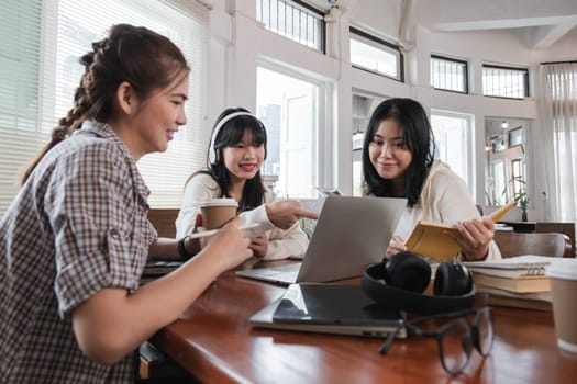 A group of cheerful Asian college students are enjoying talking and discussing their group project while sitting in a coffee shop together..