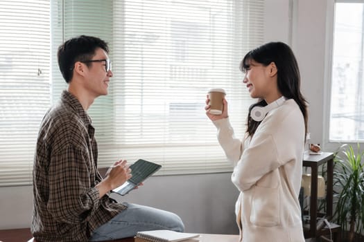 A happy young Asian man and a pretty girl are working on a laptop together, working on a co-project, sharing ideas and discussing work in a room..