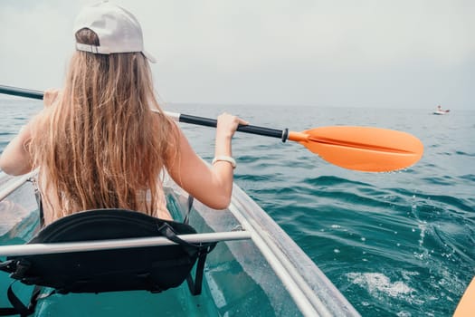 Woman in kayak back view. Happy young woman with long hair floating in transparent kayak on the crystal clear sea. Summer holiday vacation and cheerful female people having fun on the boat.