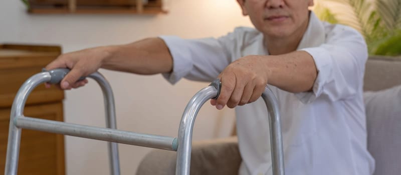 Asian woman caregiver helping senior man walking. Nurse assisting he old man patient at nursing home. Senior man using walker being helped by nurse at home. Elderly patient care and health lifestyle.