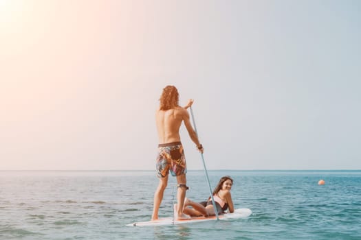 Sea woman and man on sup. Silhouette of happy young woman and man, surfing on SUP board, confident paddling through water surface. Idyllic sunset. Active lifestyle at sea or river