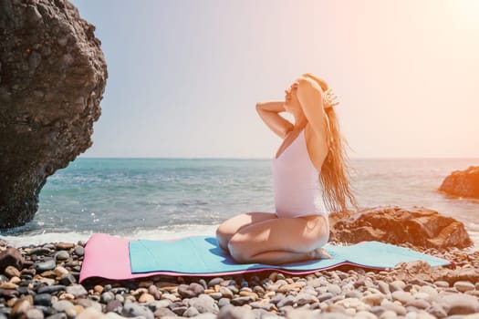 Young woman with black hair, fitness instructor in pink sports leggings and tops, doing pilates on yoga mat with magic pilates ring by the sea on the beach. Female fitness daily yoga concept