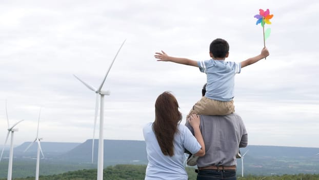 Concept of progressive happy family enjoying their time at the wind turbine farm. Electric generator from wind by wind turbine generator on the country side with hill and mountain on the horizon.