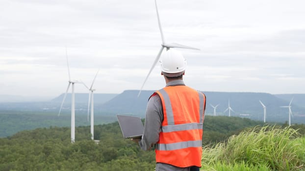 Engineer working on a wind farm atop a hill or mountain in the rural. Progressive ideal for the future production of renewable, sustainable energy. Energy generation from wind turbine.