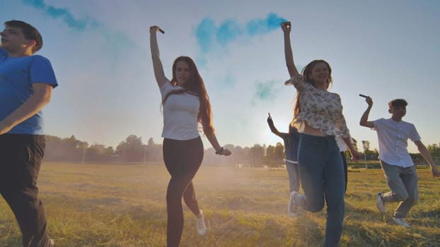 A group of friends spraying multi-colored smoke at sunset