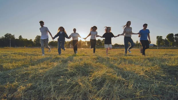 Friends running towards the sun at sunset holding hands