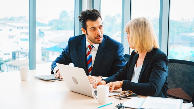 Two business people talk project strategy at office meeting room. Businessman discuss project planning with colleague at modern workplace while having conversation and advice on financial report. Jivy