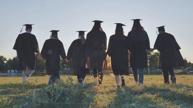 College graduates hold hands at sunset to meet the future and the sun