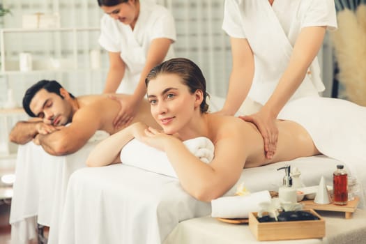 Caucasian couple customer enjoying relaxing anti-stress spa massage and pampering with beauty skin recreation leisure in day light ambient salon spa at luxury resort or hotel. Quiescent