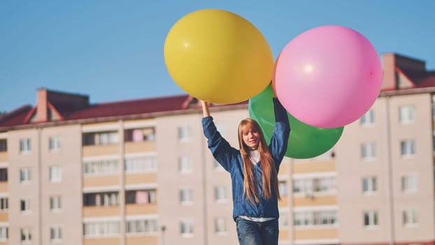 Happy girl with big with colorful balloons posing on the background of city houses