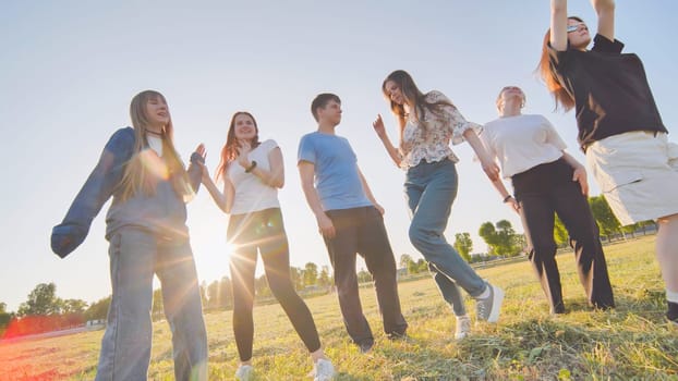 Funny jolly friends dancing in the city meadow in the evening