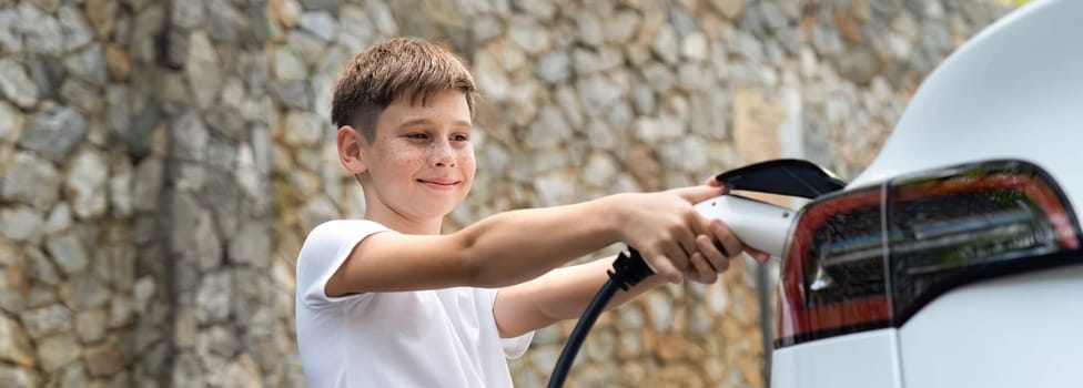 Little boy recharging eco-friendly electric car from EV charging station. EV car road trip travel concept for alternative transportation powered by clean renewable and sustainable energy. Perpetual