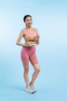 Young sporty Asian woman in sportswear holding salad bowl fill with vibrant of fruit and vegetable. Natural youthful and fit body lifestyle with balance nutrition on isolated background. Vigorous